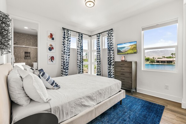 A bedroom with a bed, a dresser, a TV, and a window with a view of a landscape.