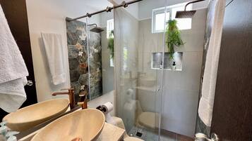 Une salle de bain avec deux lavabos, une douche dotée d’une porte en verre et un miroir agrémenté d’un pare-splash en mosaïque à motifs floraux.