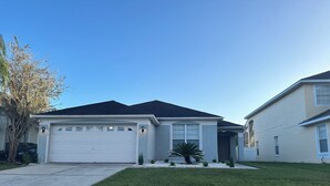 A single-story house with a garage, a small front yard with a palm tree, and a clear blue sky.
