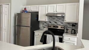 A modern kitchen with white cabinets, a stainless steel refrigerator, a black stove, and a tiled backsplash.