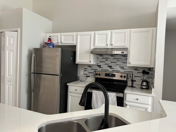 A modern kitchen with white cabinets, a stainless steel refrigerator, a black stove, and a tiled backsplash. - Beautiful Pool Family House 4/2 in Kissimmee near to Disney/Universal. (Kissimmee)