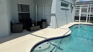 A pool area with a curved edge, outdoor furniture, and a covered section with windows.