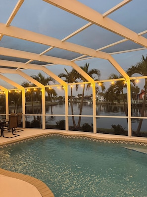 A pool area with a glass enclosure, palm trees, and string lights.