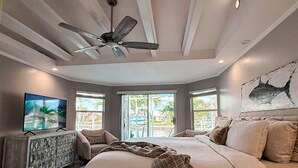 Ein Schlafzimmer mit einem Bett, einem Deckenventilator, einem Fernseher und einem großen Fenster.