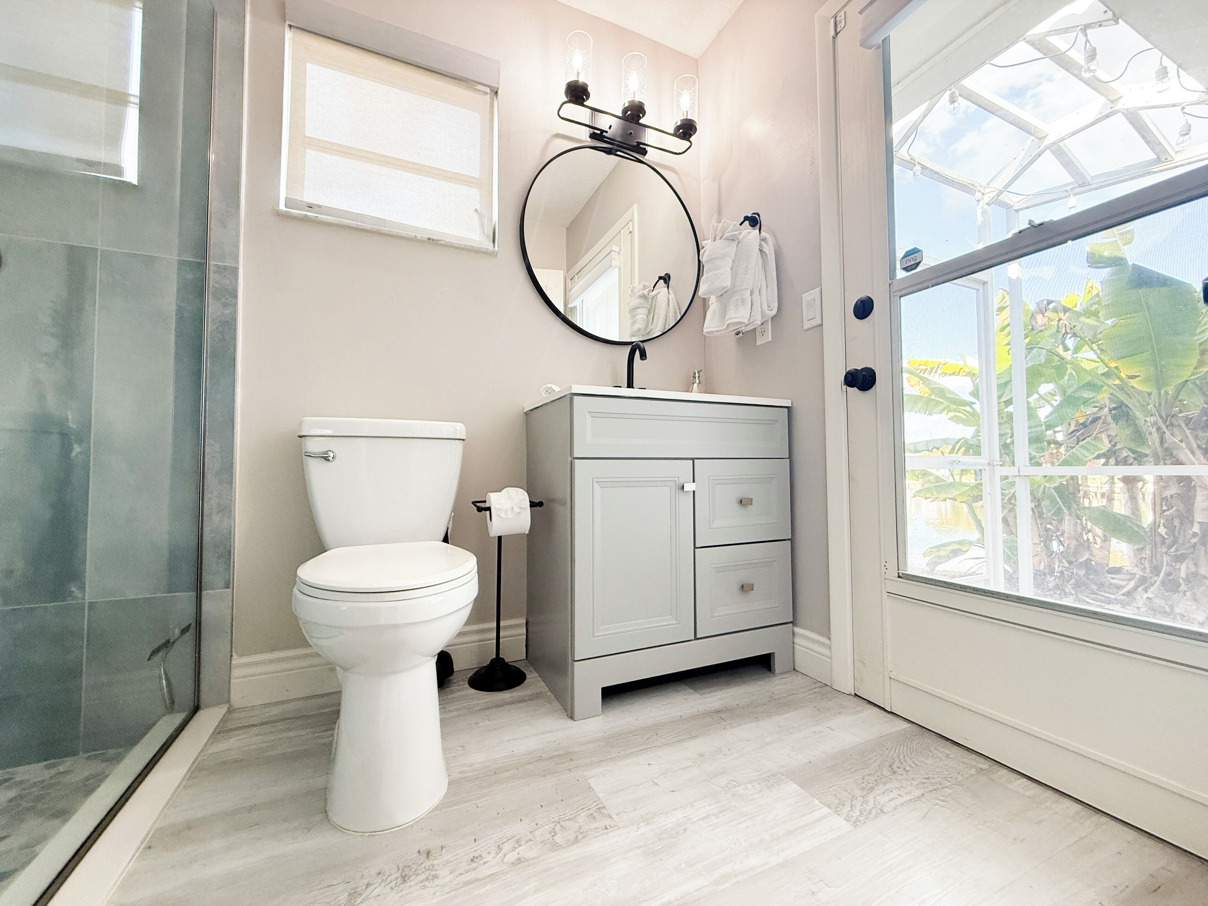 Une salle de bain comprenant des toilettes, un lavabo, un miroir et une fenêtre donnant sur un espace verdoyant.