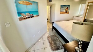 A bedroom with a bed, a lamp, a painting of a beach scene, and a rug.