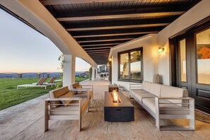 An outdoor seating area with a fire feature, a sofa, and a view of a green landscape.