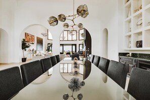 A modern dining area with a long table, black upholstered chairs, and a unique chandelier.