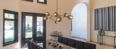 A modern dining area with a long table, dark chairs, and a unique chandelier.