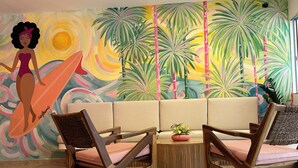 A room with a sofa, two wooden chairs, a small table with a plant, and a colorful mural with a tropical theme. - Hotel Taybo Kai By St Hoteles (Santa Marta)