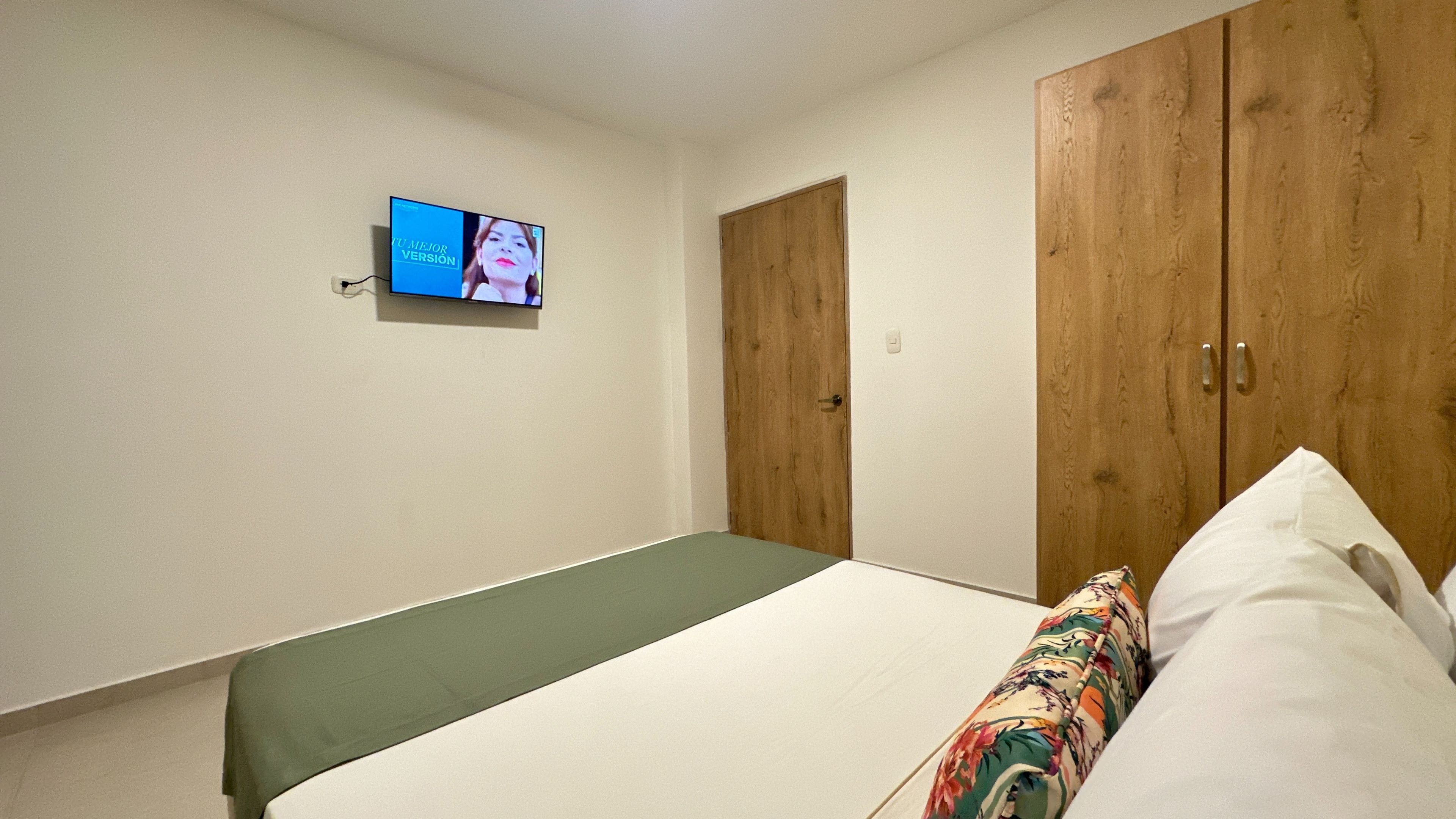 A bedroom with a single bed, a wooden wardrobe, and a television on the wall.