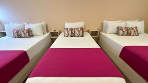 A hotel room with three single beds, each with a white pillow and a floral pillow. The beds have white bedding and a magenta bedspread. There are wooden nightstands between the beds. - Hotel Taybo Kai By St Hoteles (Santa Marta)