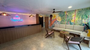 Zona de recepción de un hotel con un letrero de neón, un mural, un sofá y mobiliario de madera.