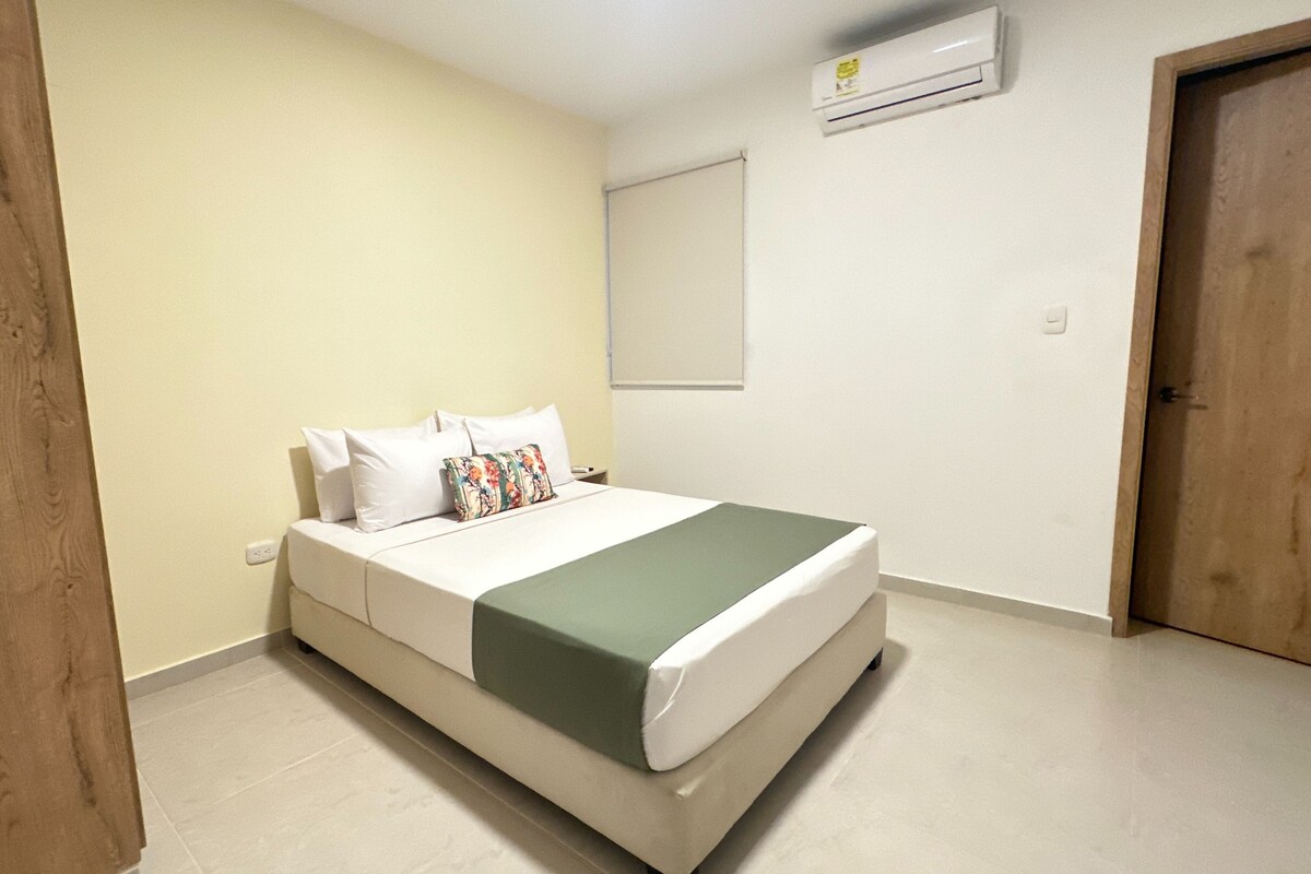 A bedroom with a bed, a wooden door, a white wall, and a white ceiling.