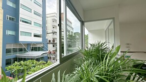 A room with a large window, a balcony with plants, and a view of neighboring buildings. - Hotel Taybo Kai By St Hoteles (Santa Marta)