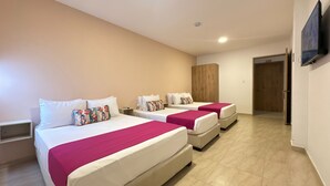 A hotel room with three beds, each with white bedding and a pink bedspread. There is a wooden wardrobe and a television mounted on the wall. - Hotel Taybo Kai By St Hoteles (Santa Marta)