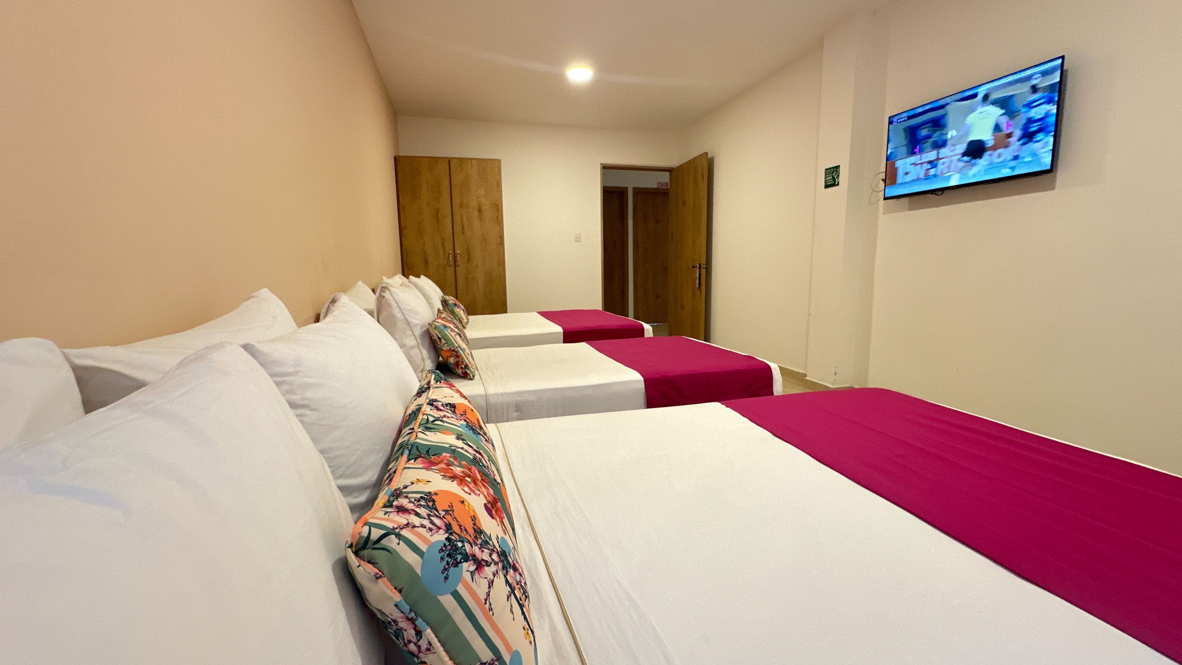 A hotel room with two beds, each with white bedding and a pink bedspread. There is a television mounted on the wall displaying a sports event.