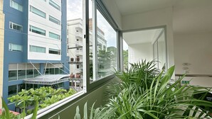 A room with a large window, a balcony with plants, and a view of neighboring buildings. - Hotel Taybo Kai By St Hoteles (Santa Marta)