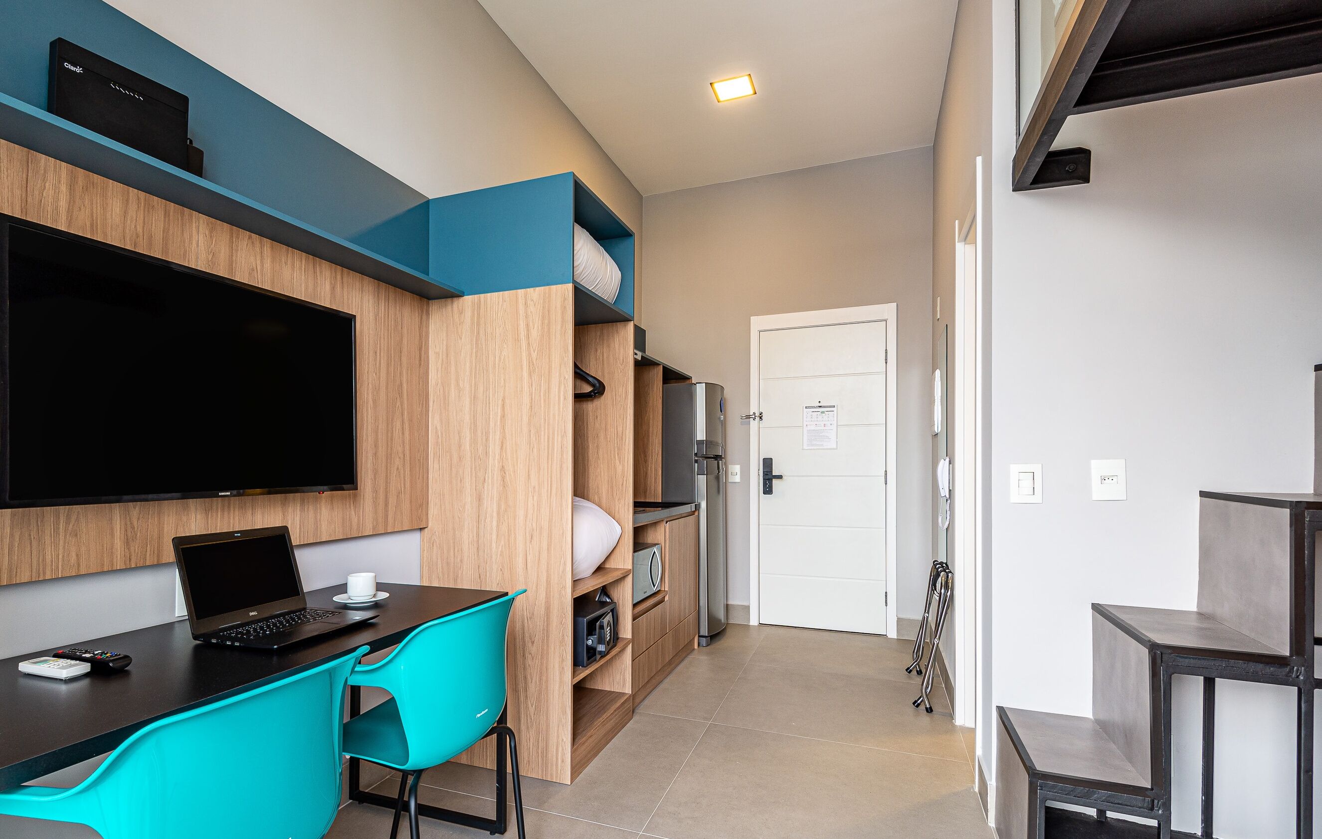 A compact room with a bed, a desk with a laptop, a TV, and a coffee table.
