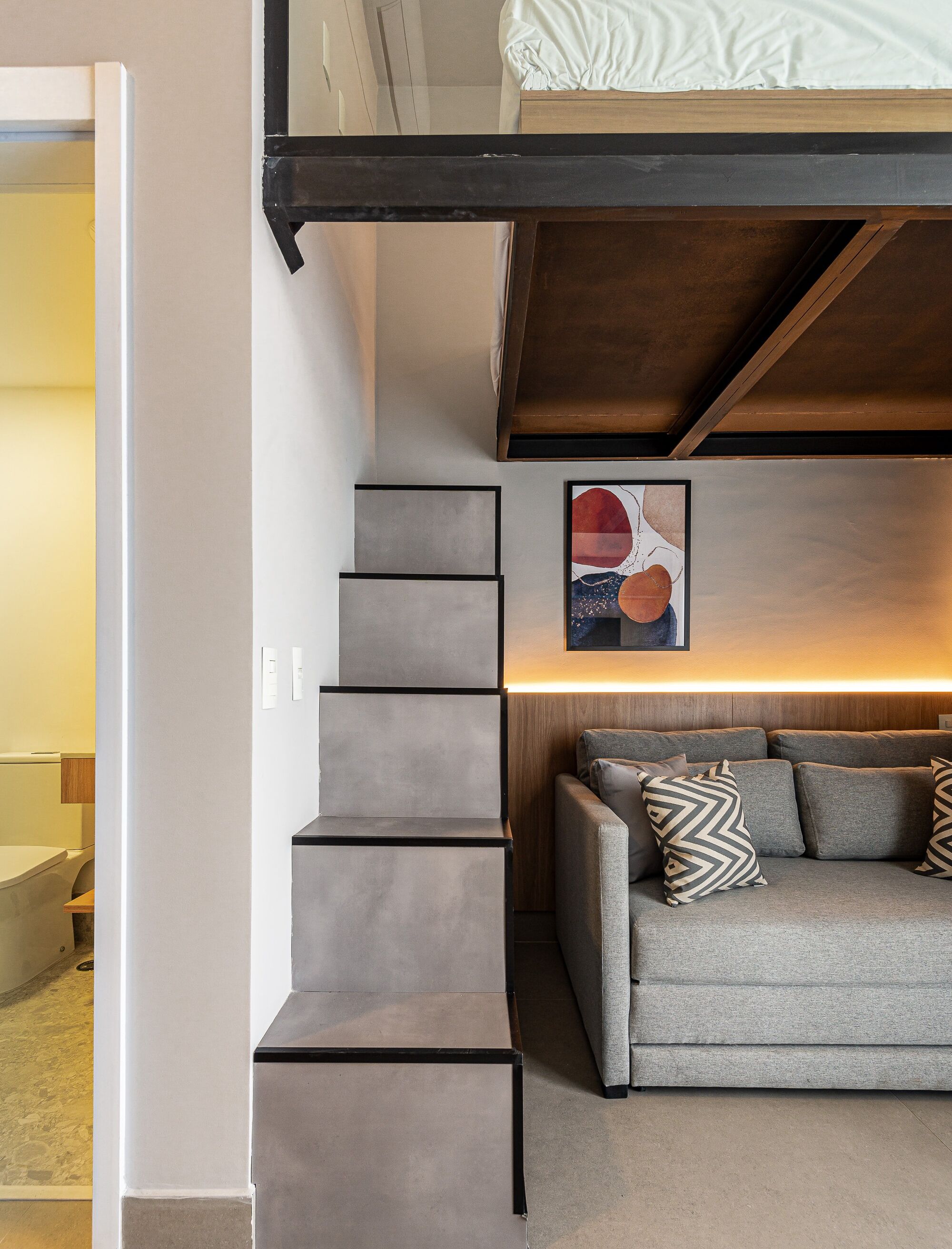 Um interior moderno com escada, sofá com almofadas estampadas e uma obra de arte emoldurada na parede.