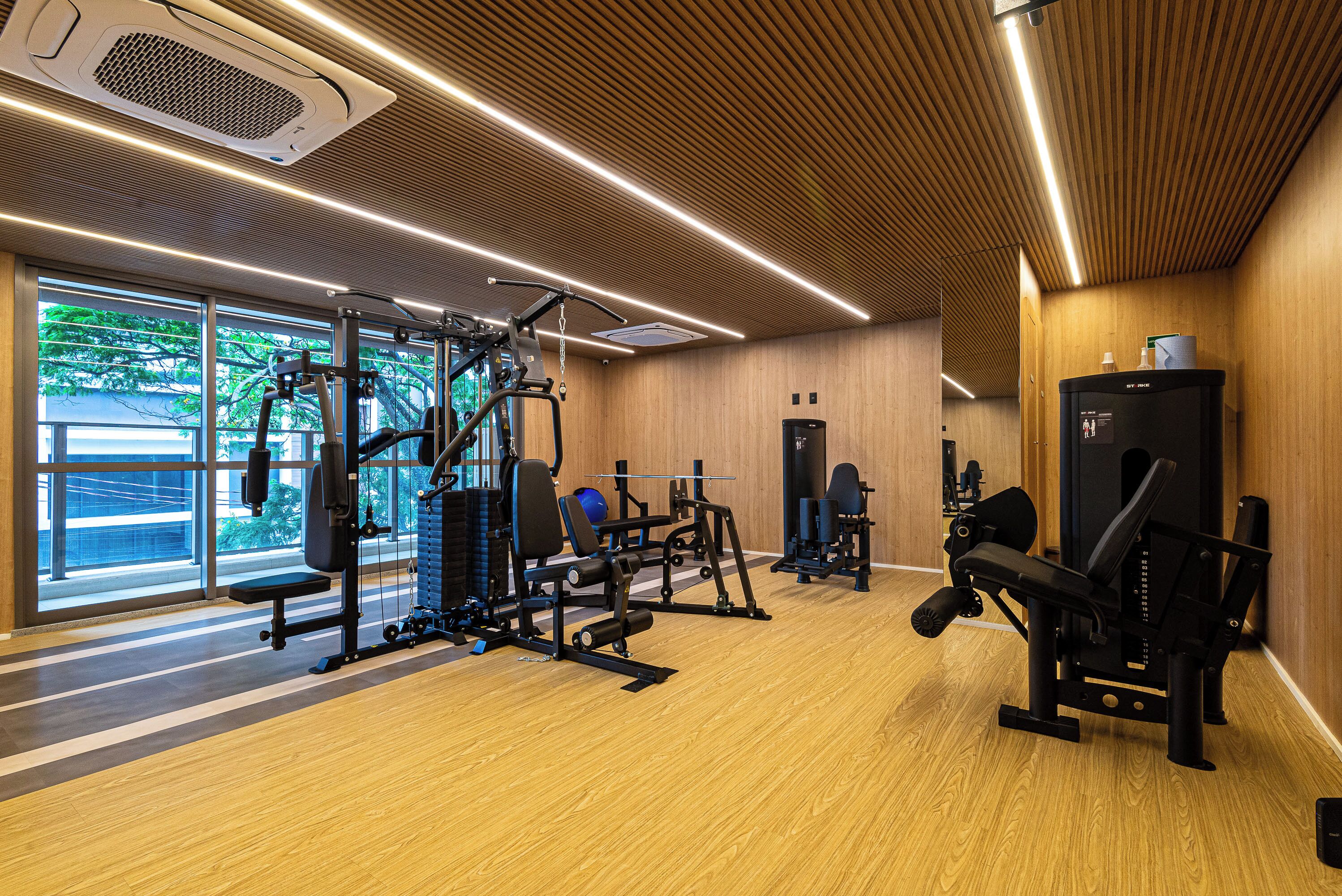 Een sportschool met fitnessapparatuur, grote ramen en een houten vloer.