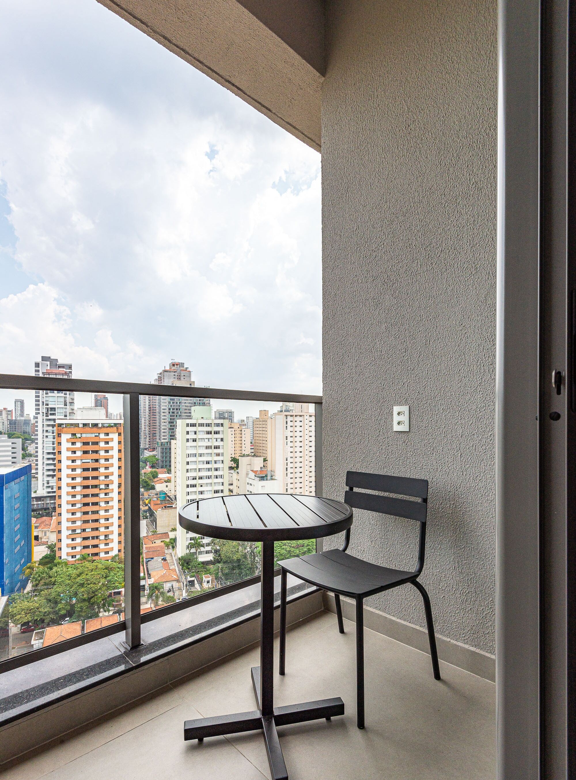 Un balcon avec une table et une chaise, un mur à la texture intéressante et une vue sur la ville.