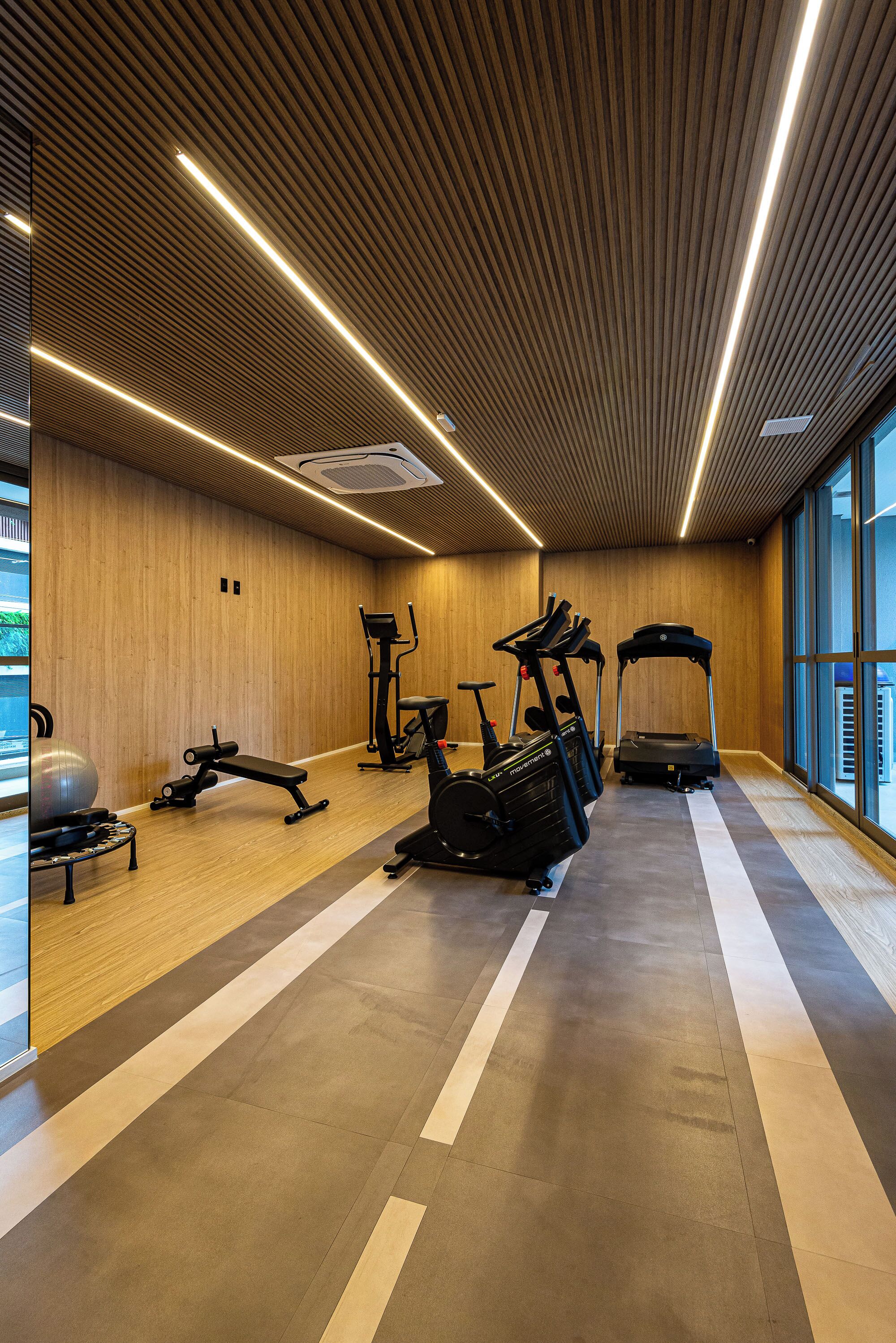 A gym with exercise equipment, wooden walls, and large windows.