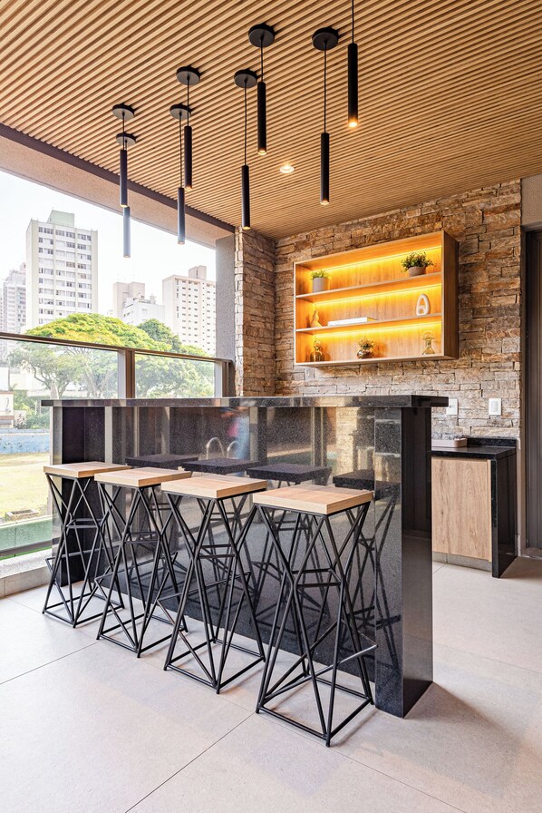 A modern bar area with a stone wall, wooden shelves, and a large window overlooking a cityscape.