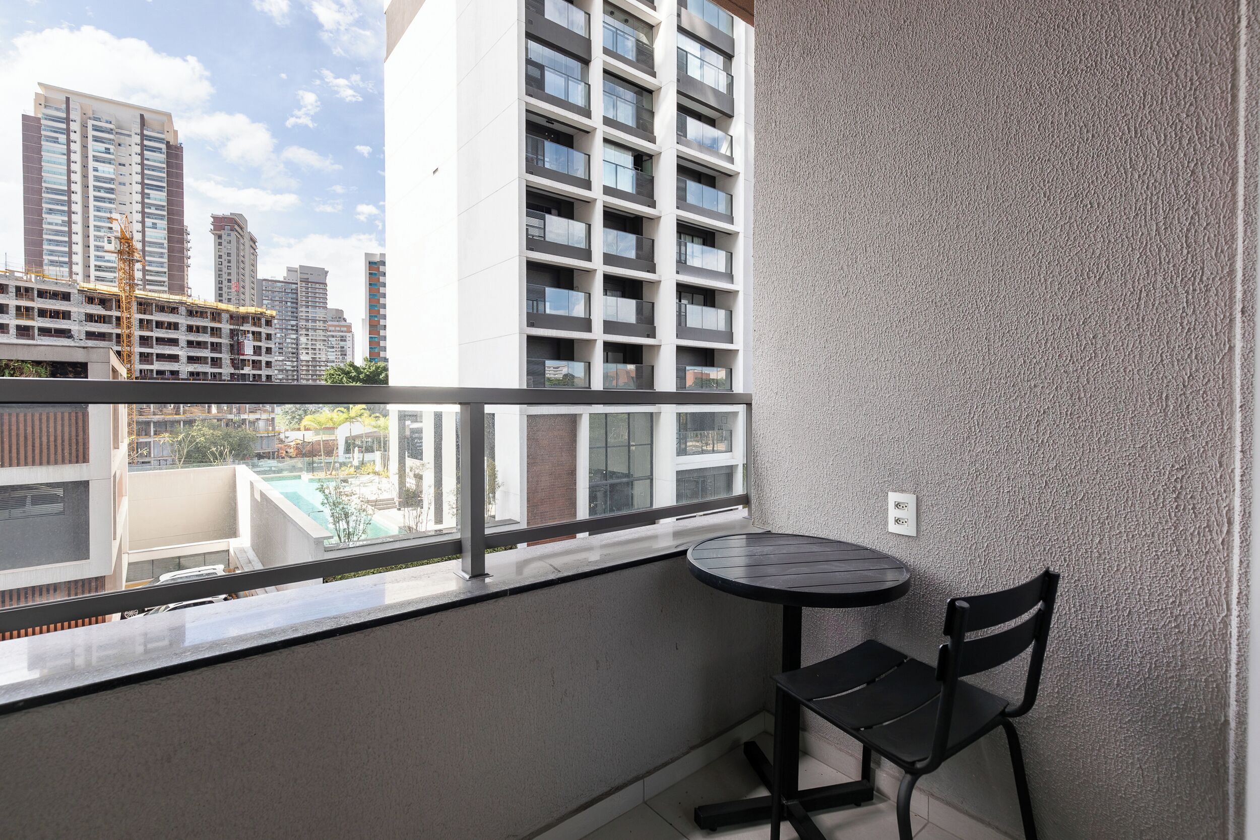 Un balcon avec une table et des chaises, donnant sur un paysage urbain avec des bâtiments modernes.