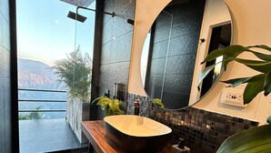 Ein modernes Badezimmer mit einem großen Holzbadezimmer-Möbel, einem runden Spiegel und Blick auf Berge durch ein großes Fenster.
