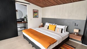 Ein modernes Schlafzimmer mit einem großen Bett, einem Deckenventilator, einem Nachttisch und einem durch eine Schiebetür einsehbaren Badezimmer.