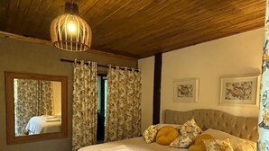 A bedroom with a large bed, wooden ceiling, floral curtains, and a mirror.