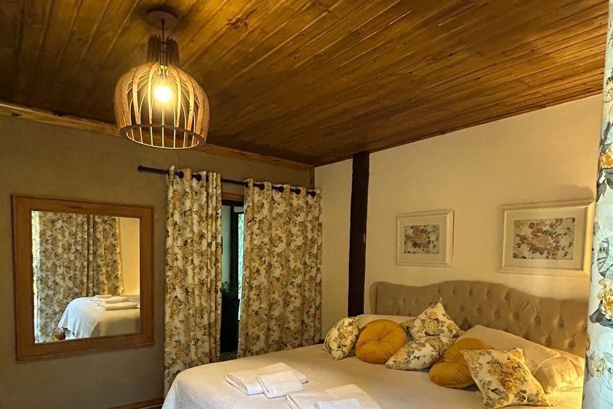 Quarto com cama grande, teto de madeira, cortinas florais e um espelho.