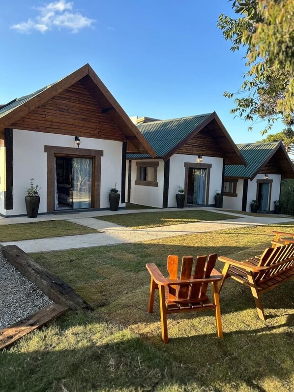 Un edificio moderno con fachada blanca y detalles de madera, que cuenta con un área de estar exterior cubierta con sillas de madera.