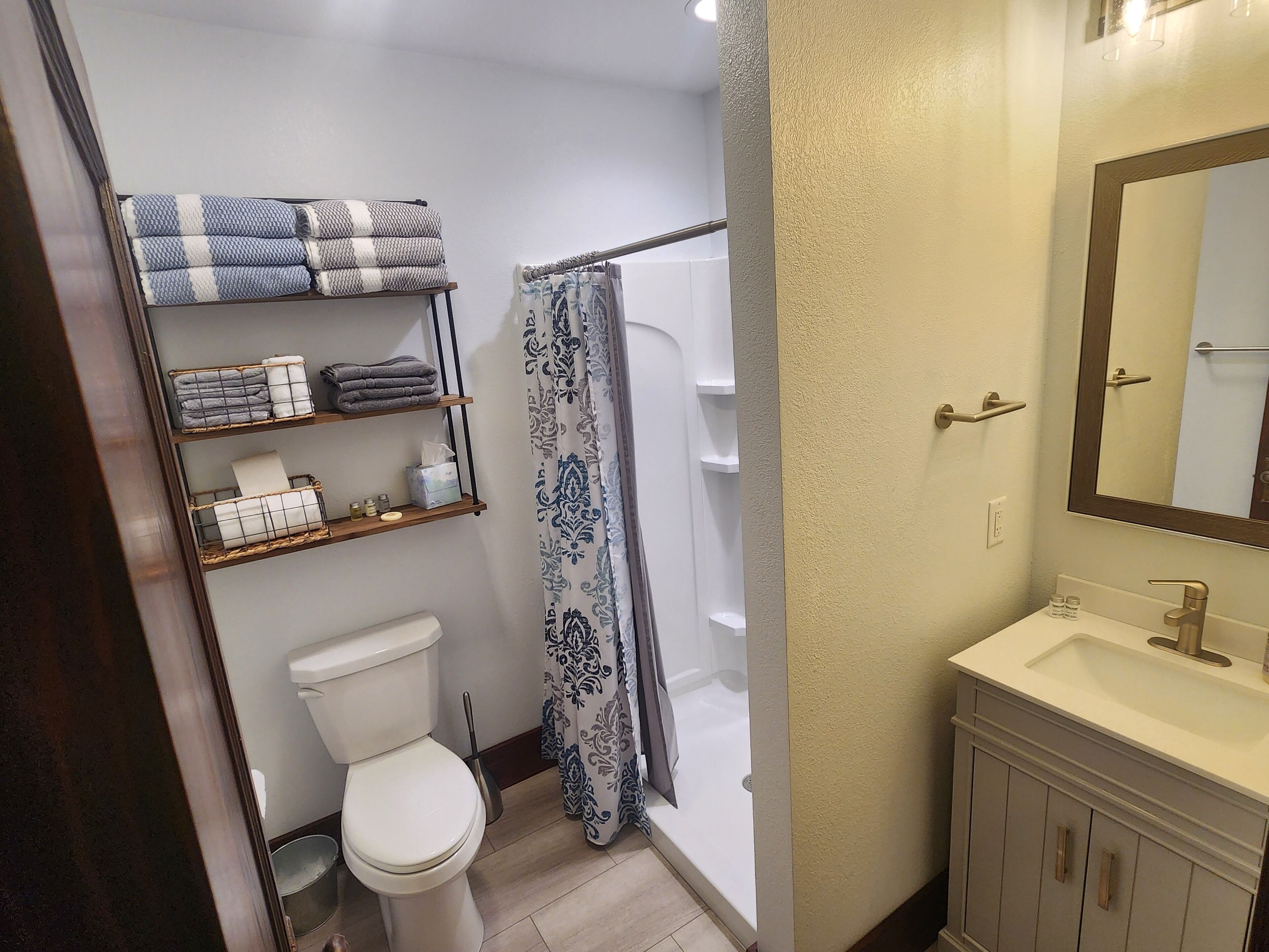 Un bagno con il water, una doccia, un lavandino e scaffali con asciugamani e articoli da toilette.