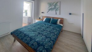 A bedroom with a bed, a nightstand, a wall-mounted lamp, and a window with a view of a balcony.