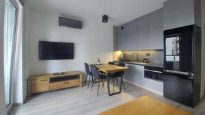A modern kitchen with a dining area, including a wooden table, chairs, and a TV mounted on the wall.