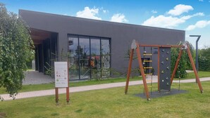 A modern building with a glass entrance, a wooden climbing structure, and a signboard in front.