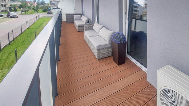 A balcony with a wooden floor, a sofa, and a planter with flowers.