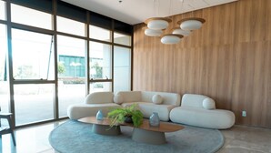 A modern living room with a large window, a white sofa, a round coffee table with decorative items, and a wooden accent wall. - Roomo Transamerica Recife Parque do Cais (Recife)
