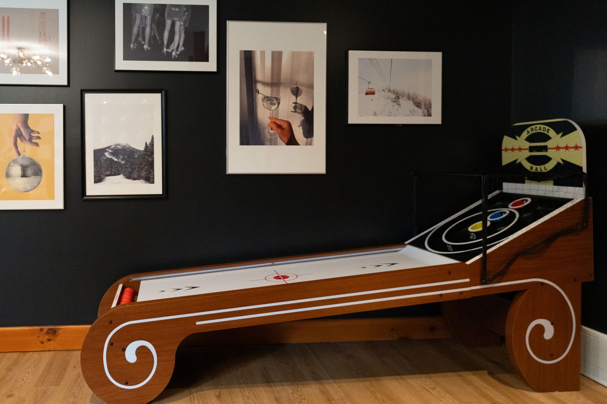 A room with a wooden bed, framed pictures on the wall, and a wooden arcade ball table.