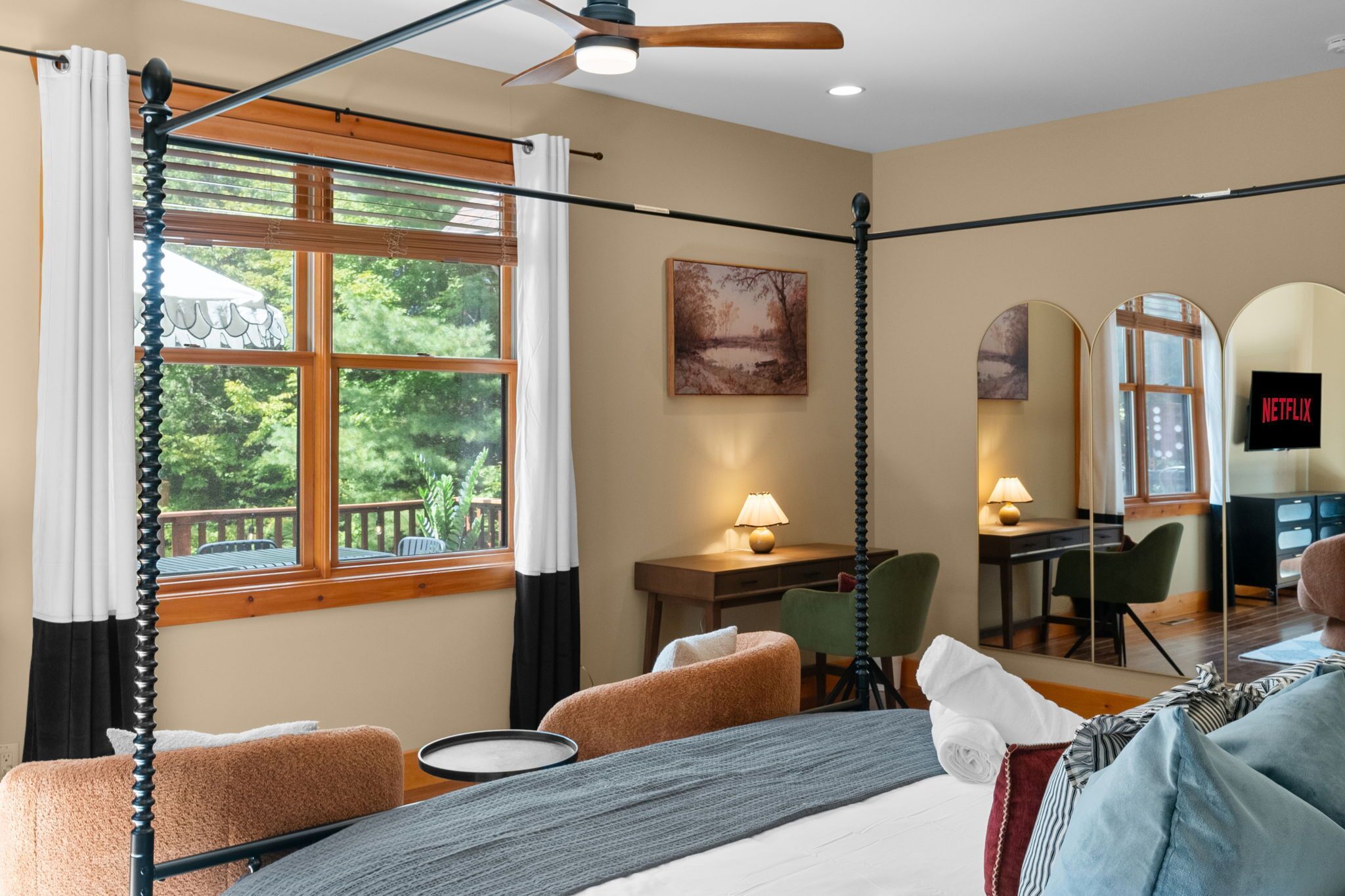 Ein Zimmer mit einem Bett, einem Schreibtisch, einem Sessel, einem Fernseher und einem fenster mit Vorhängen.