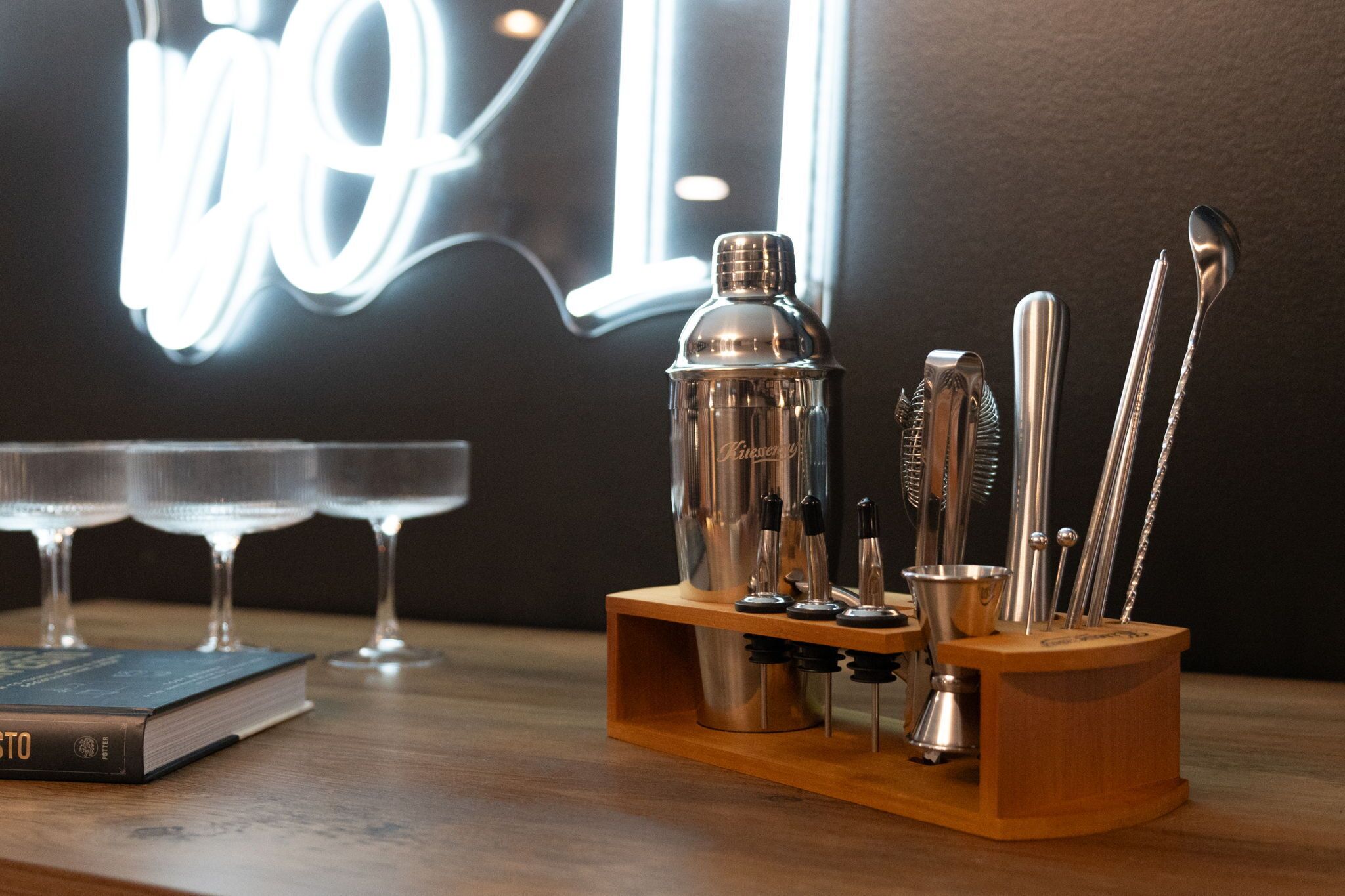 A bar area with a cocktail shaker, jigger, strainer, and other bartending tools on a wooden stand.