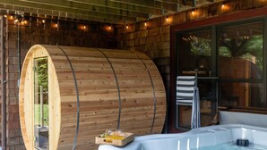 A wooden sauna with a glass door, a hot tub, and a wooden deck with string lights. - Luxury Chalet, Firepit, Sauna, Pet Friendly, 5 mins to Windham Mtn resort (Windham)