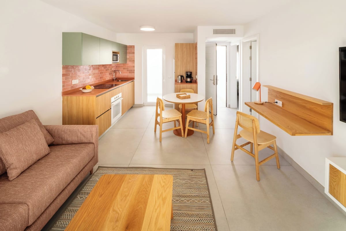 A modern living space with a sofa, dining table, chairs, a coffee machine, and a TV.