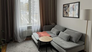 Un salon moderne avec un canapé gris, une petite table d’appoint ronde en bois et un tableau abstrait encadré accroché au mur.