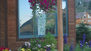 Ein Holzhaus mit großen Fenstern und einer Veranda, die mit verschiedenen Blumentöpfen und Blumen geschmückt ist.