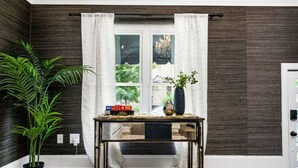 A room with dark wood paneling, a window with white curtains, a small table with books and a vase, and a potted plant. - Luxe Studio w/ King Bed + Sofa | Walk to OSU/Bars (Columbus)