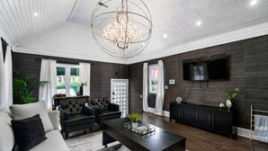 A modern living room with a chandelier, dark wood flooring, a sofa, and a TV mounted on the wall. - Luxe Studio w/ King Bed + Sofa | Walk to OSU/Bars (Columbus)