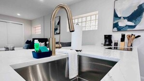 Een moderne keuken met een roestvrijstalen spoelbak, witte marmeren aanrechtbladen en een strakke kraan.